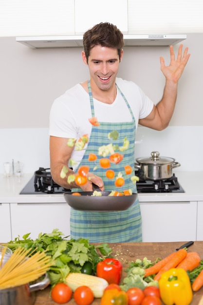 Uomo allegro che getta le verdure in cucina