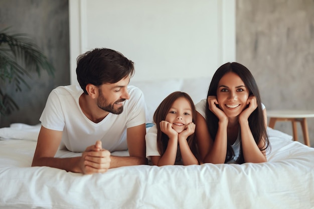 Uomo allegro che guarda felicemente sua moglie e la loro figlia sdraiati sul letto