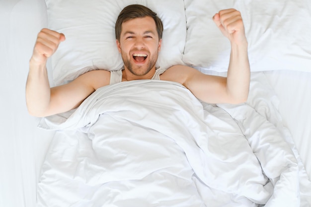 Uomo allegro che si sveglia sdraiato in un letto accogliente a casa il concetto di sonno sano di mattina di fine settimana