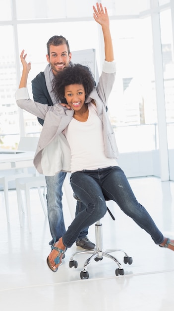 Uomo allegro che spinge donna sulla sedia in ufficio