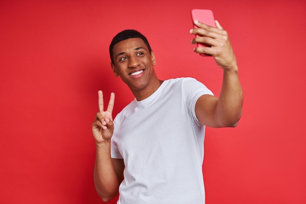Uomo allegro di razza mista che utilizza lo smartphone mentre si trova su sfondo rosso