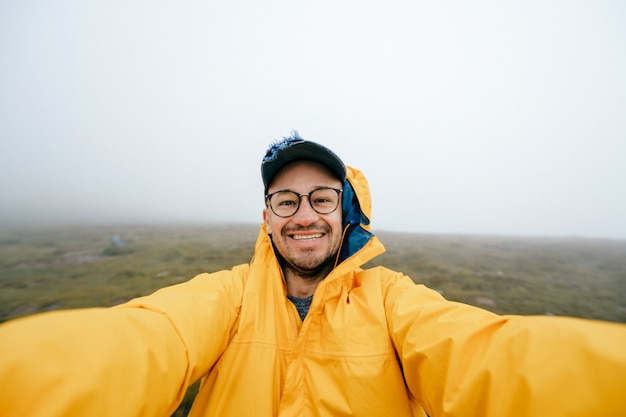 Uomo allegro felice che prende selfie in montagna nebbiosa ventosa