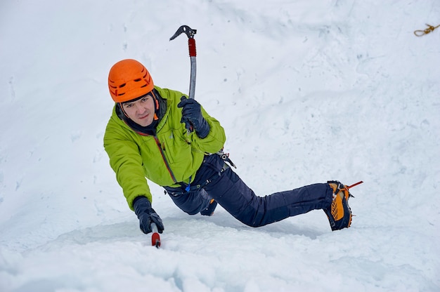 Uomo alpinista con ascia strumenti di ghiaccio nel casco arancione arrampicata su una grande parete di ghiaccio. Ritratto di sport all'aperto.