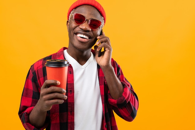 Uomo americano nero alla moda in camicia rossa a quadretti con bicchiere di caffè su giallo