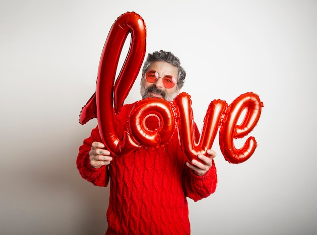Uomo amichevole con gli occhiali in possesso di un palloncino rosso con la parola amore su sfondo bianco.