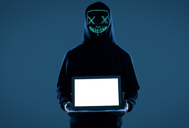Uomo anonimo con un cappuccio nero e una maschera al neon che si intrufola in un computer.