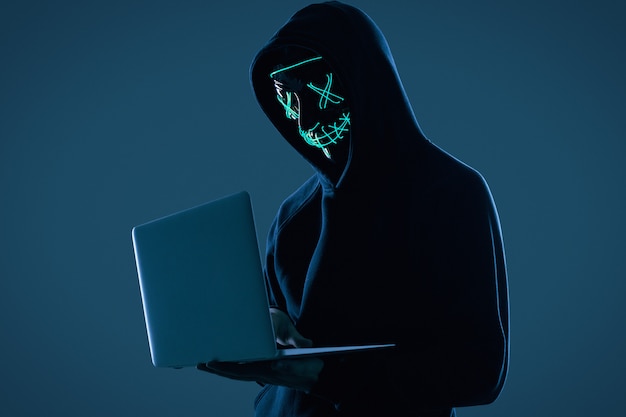 Uomo anonimo in felpa con cappuccio nera e maschera al neon che hackerano un computer