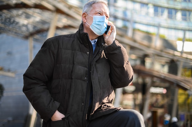 Uomo anziano al telefono all'aperto che indossa una maschera, concetto di coronavirus