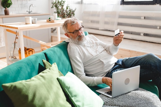 Uomo anziano anziano che effettua pagamenti online utilizzando il laptop Vecchio nonno che fa shopping e-commerce con carta di credito Pensionato in possesso di carta di debito per l'internet banking Copia spazio e luogo pubblicità