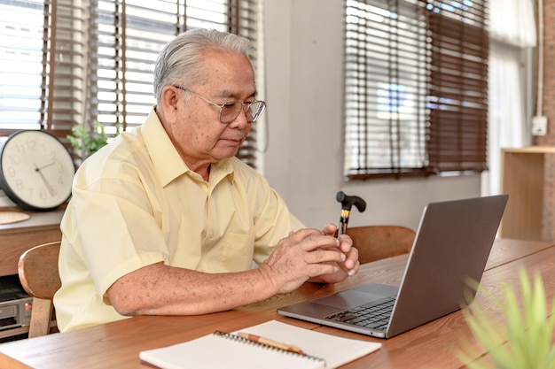 Uomo anziano asiatico che usa il computer portatile e cerca l'assicurazione dopo il pensionamento. Il nonno resta solo a casa.