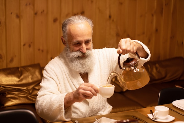 Uomo anziano barbuto bere il tè dopo la procedura nella sauna. Concetto - stile di vita sano.