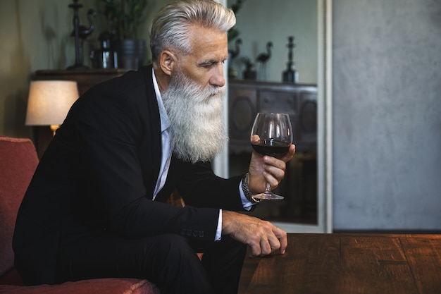 Uomo anziano barbuto elegante e bello che beve vino rosso