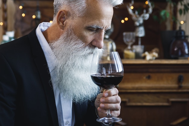 Uomo anziano barbuto elegante e bello che beve vino rosso