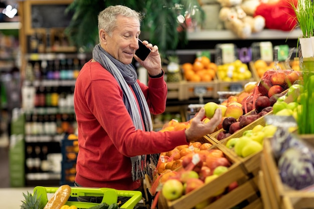 Uomo anziano bello che ha conversazione telefonica durante lo shopping