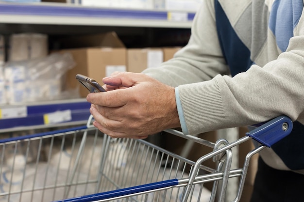 Uomo anziano che fa shopping al supermercato con lo smartphone Primo piano di handsxDxA