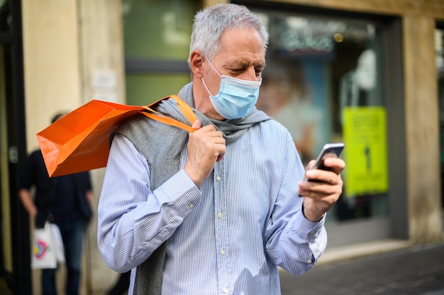 Uomo anziano che fa shopping all'aperto ai tempi del coronavirus, indossando maschere