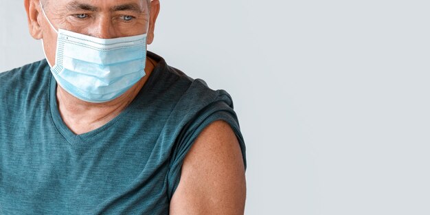 Uomo anziano che indossa una maschera protettiva si prepara per l'iniezione. Uomo Anziano In Clinica, Ospedale. Vaccinazione degli anziani. Vaccino contro il coronavirus COVID 19 per uomo maturo. Protezione del paziente anziano.