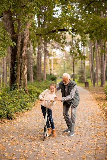 Uomo anziano che insegna a sua nipote come guidare il monopattino nel parco