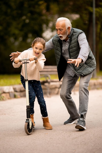 Uomo anziano che insegna a sua nipote come guidare il monopattino nel parco