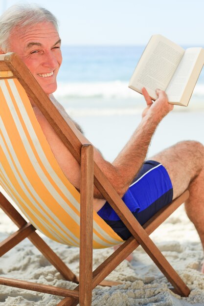 Uomo anziano che legge un libro in spiaggia