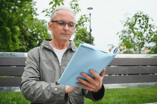 Uomo anziano che legge un libro nel parco