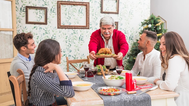Uomo anziano che mette pollo al forno sulla tavola festiva
