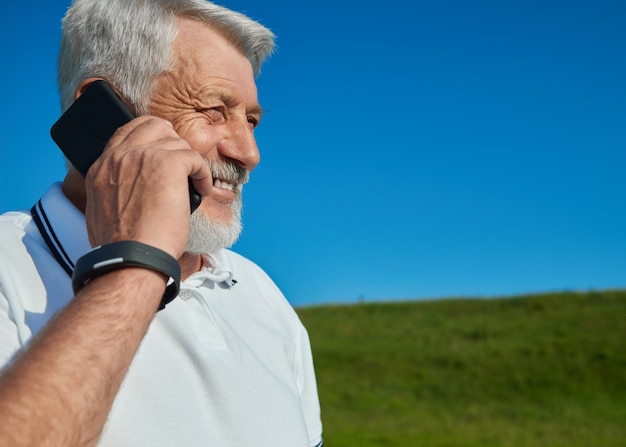 Uomo anziano che parla sul telefono cellulare nel campo.