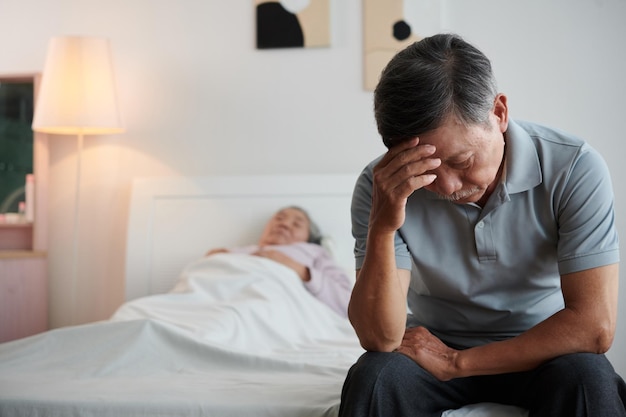 Uomo anziano che piange seduto sul letto della moglie