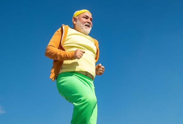 Uomo anziano che pratica sport su sfondo blu cielo allegro senior jogging in abiti sportivi su sky ba...