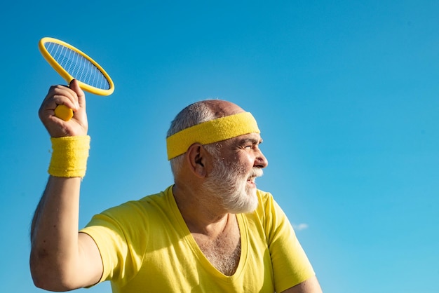 Uomo anziano che pratica tennis su sfondo blu cielo giocatore di tennis uomo anziano che serve