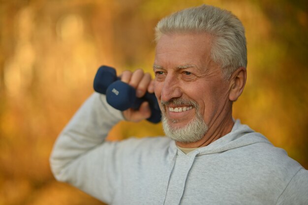 Uomo anziano che si esercita con i manubri nel parco autunnale