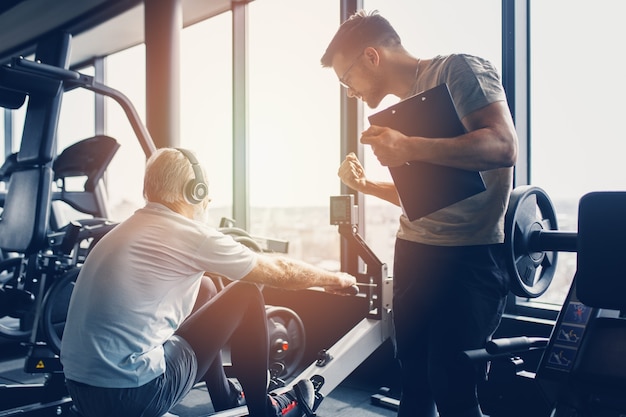 Uomo anziano che si esercita in palestra con il suo personal trainer.