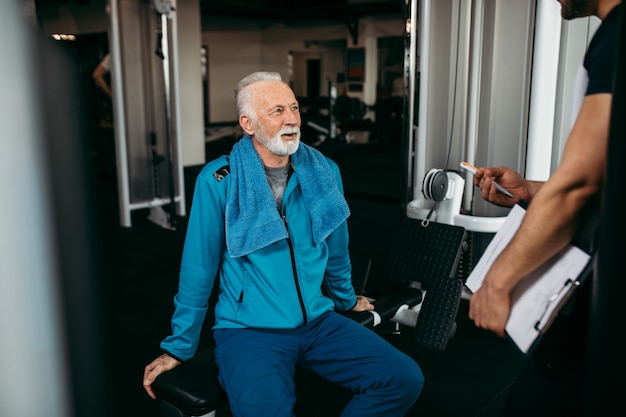 Uomo anziano che si esercita in palestra con il suo personal trainer.