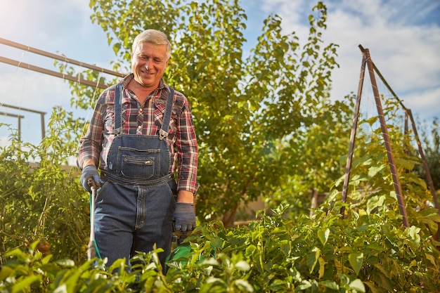 Uomo anziano che sorride mentre lavora nel suo giardino e spruzza le sue piante