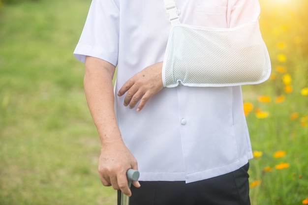 Uomo anziano che tiene un braccio rotto della canna dopo l'incidente con la stecca del braccio di usura nel parco