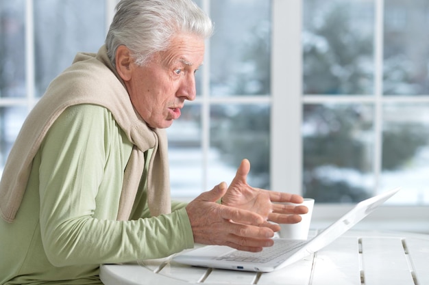Uomo anziano che usa il laptop seduto vicino alla finestra