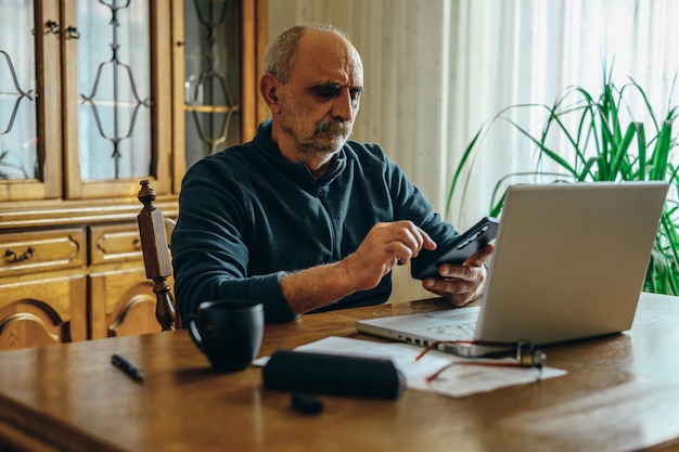 Uomo anziano che utilizza un laptop e uno smartphone a casa