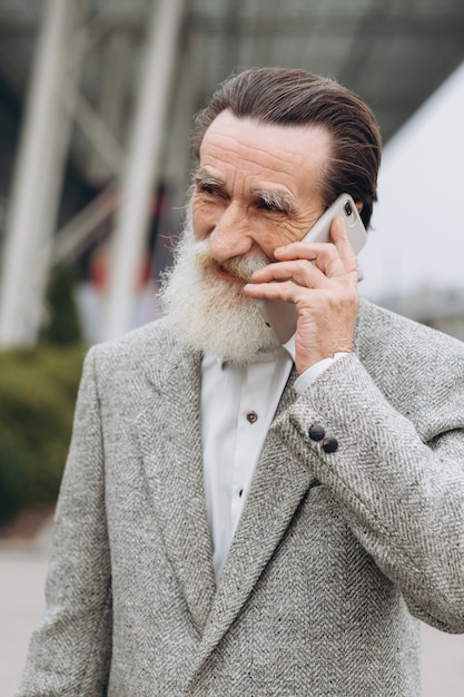 Uomo anziano con barba grigia e baffi in una giacca parla al telefono