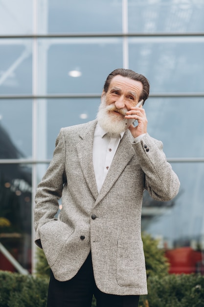 Uomo anziano con barba grigia e baffi in una giacca parla al telefono