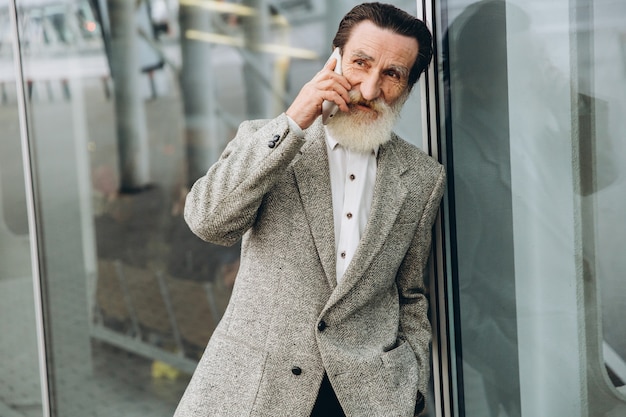 Uomo anziano con barba grigia e baffi in una giacca parla al telefono
