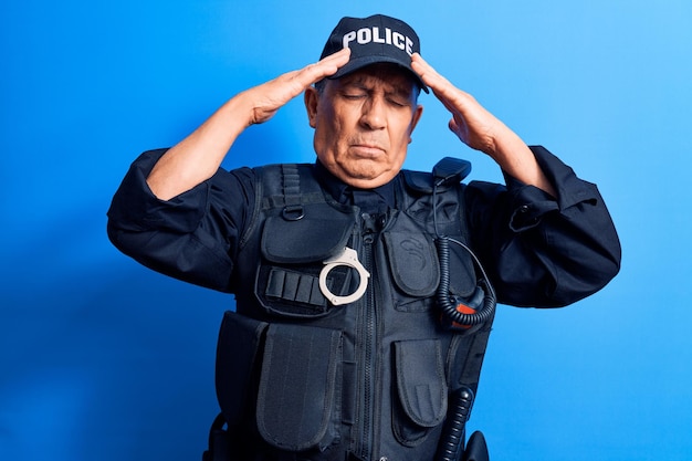 Uomo anziano con i capelli grigi che indossa l'uniforme della polizia con la mano sulla testa, mal di testa a causa dello stress. soffre di emicrania.