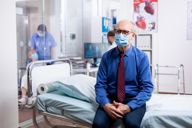 Uomo anziano con maschera facciale contro il covid in attesa di consultazione medica nel gabinetto dell'ospedale