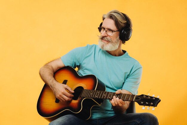 Uomo anziano con occhiali e cuffie che suona la chitarra su sfondo giallo Riprese in studio