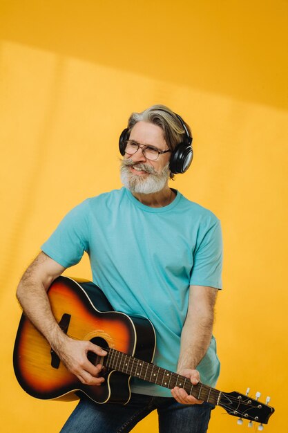 Uomo anziano con occhiali e cuffie che suona la chitarra su sfondo giallo Riprese in studio