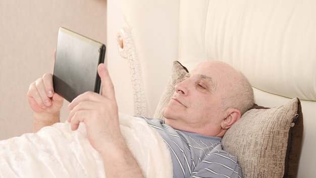 Uomo anziano con tavoletta sul letto.