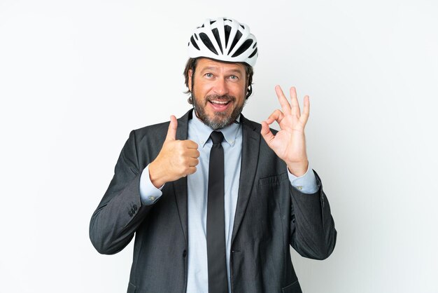 Uomo anziano d'affari con un casco da bici isolato su sfondo bianco che mostra segno ok e gesto pollice in alto