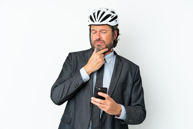 Uomo anziano d'affari con un casco da bici isolato su sfondo bianco pensando e inviando un messaggio