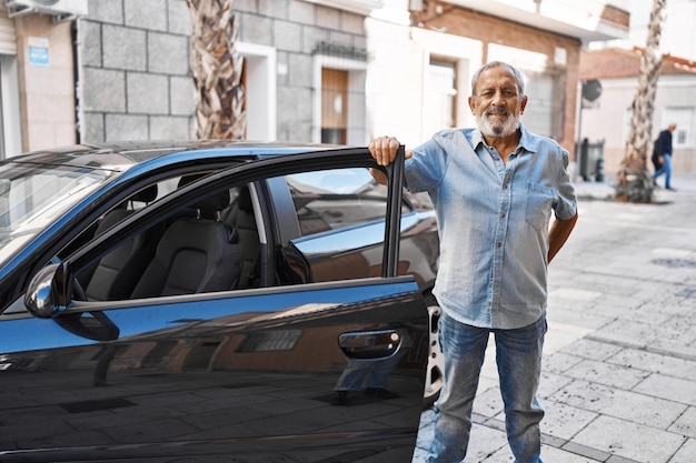 Uomo anziano dai capelli grigi che sorride fiducioso aprendo la porta dell'auto in strada