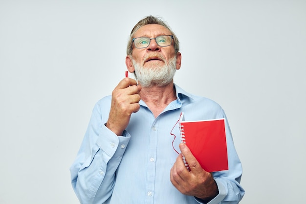 Uomo anziano dai capelli grigi con taccuino rosso e penna su sfondo chiaro