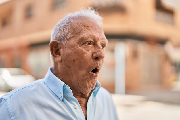 Uomo anziano dai capelli grigi in piedi con espressione sorpresa in strada